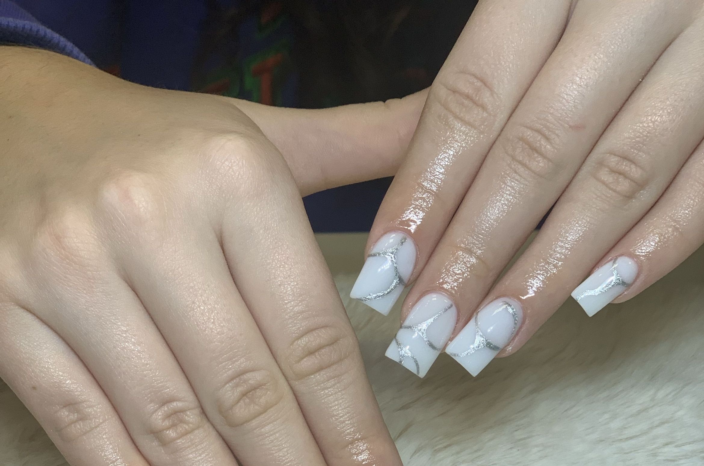 Zbliżenie na dłonie z manicure w biało-srebrnym geometrycznym wzorze